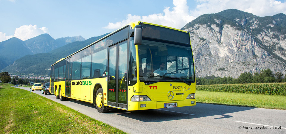 Auf dem Bild ist ein gelber Bus zu sehen. Er fährt auf einer Straße. Im Hintergrund sieht man Berge.
Foto: VVT